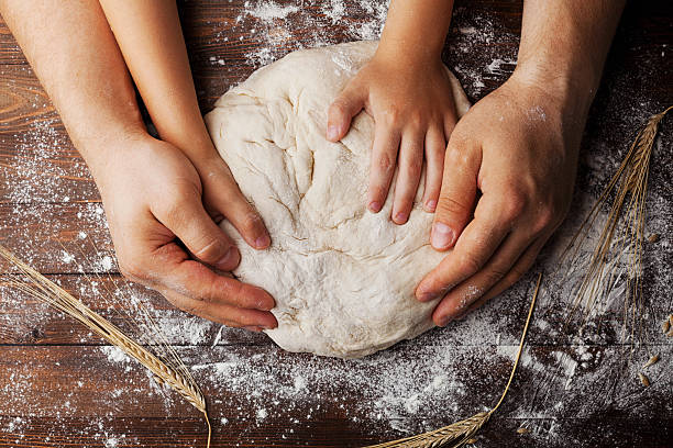 Child and adult hands kneading dough together on a floured wooden surface, symbolizing tradition, learning, and family bonding in baking.